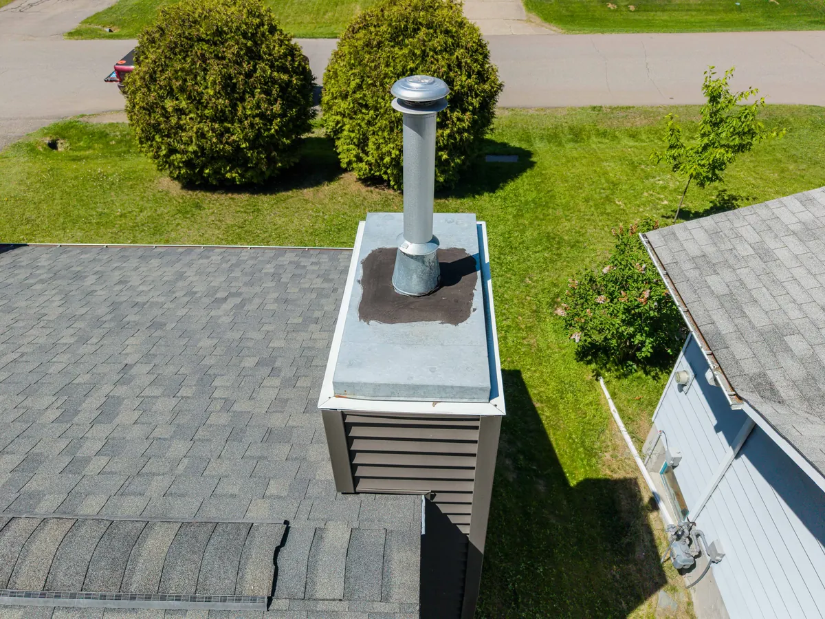 Aerial view of a roof penetration and its surrounding cap, curb, flashing, and shingles